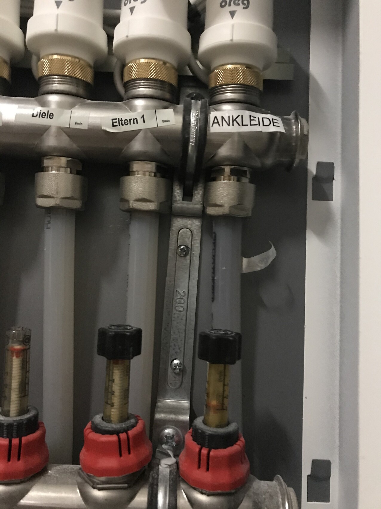 Metallischer Rohrverteiler mit Ventilen, beschrifteten Leitungen 'Eltern 1' und 'ANKLEIDE'.
