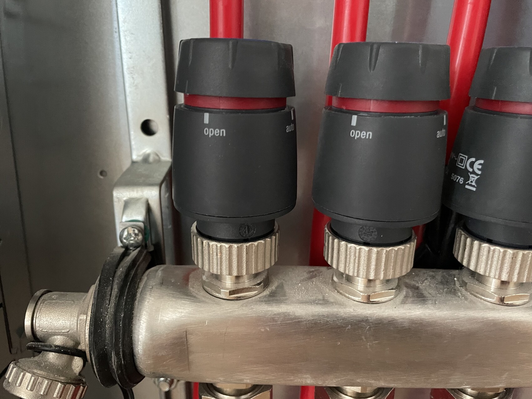 Mehrfachventilblock mit drei schwarzen Deckeln und rotem Rohr dahinter aus Metall.