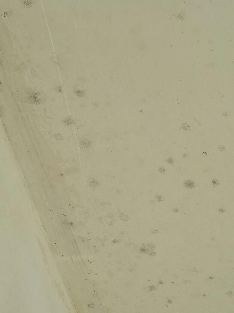Helle beige betonwand mit dunklen flecken und oberflaechenunebenheiten