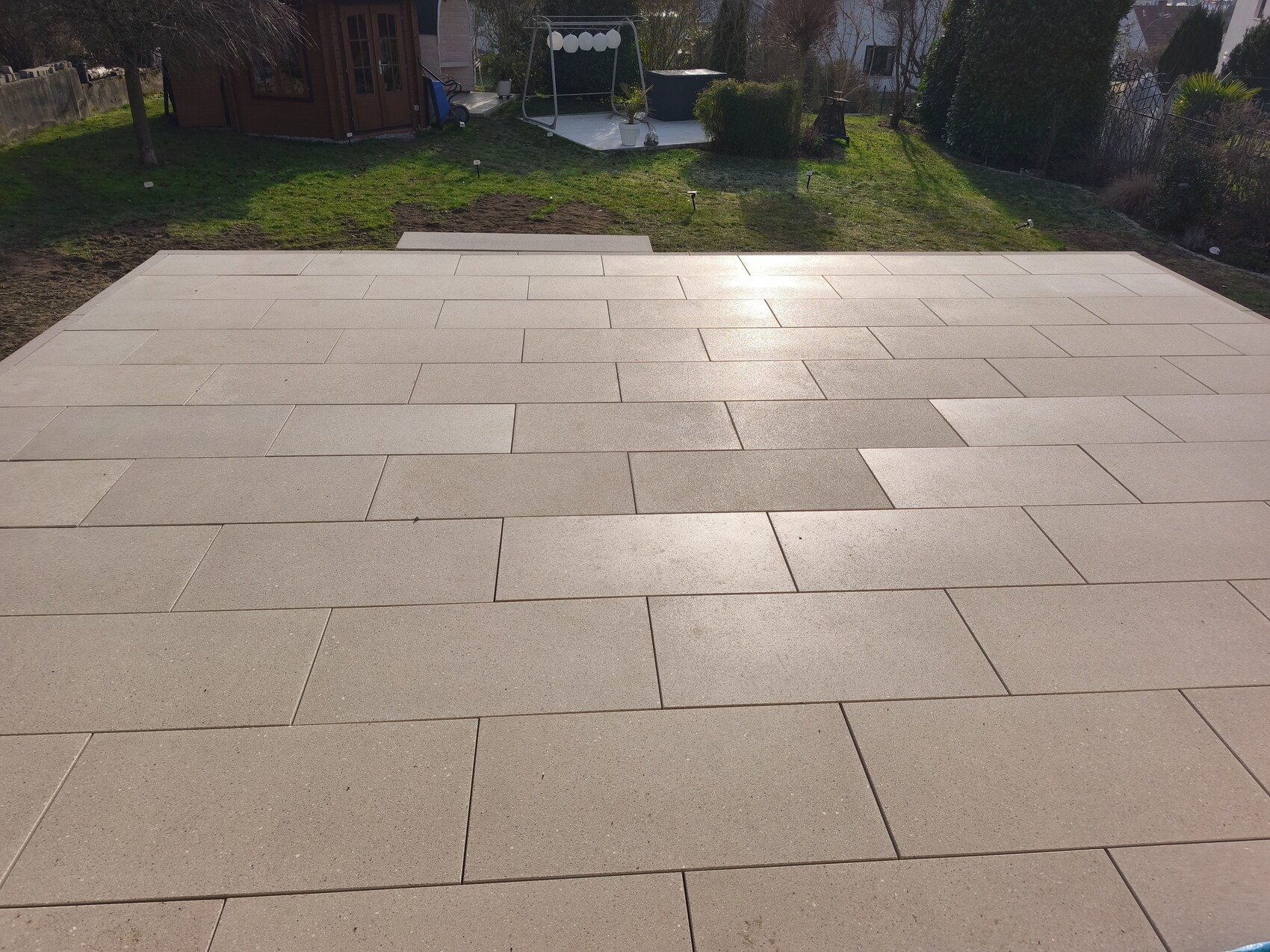 Große beige Terrassenplatten bilden eine Terrasse mit Garten im Hintergrund