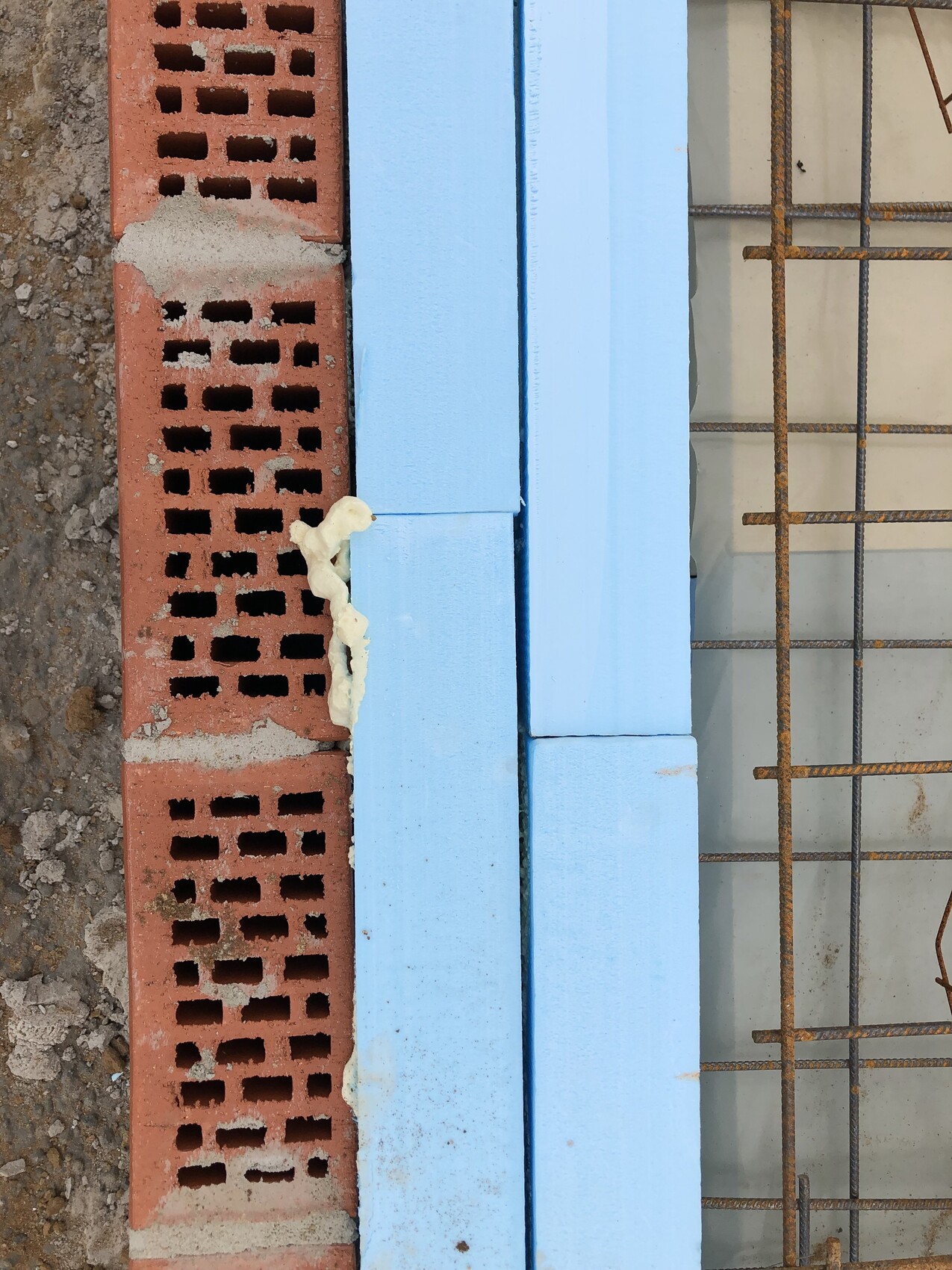 Baustelle: rote Hohlblocksteine, blaue Dämmplatten und rostige Bewehrungsstäbe.