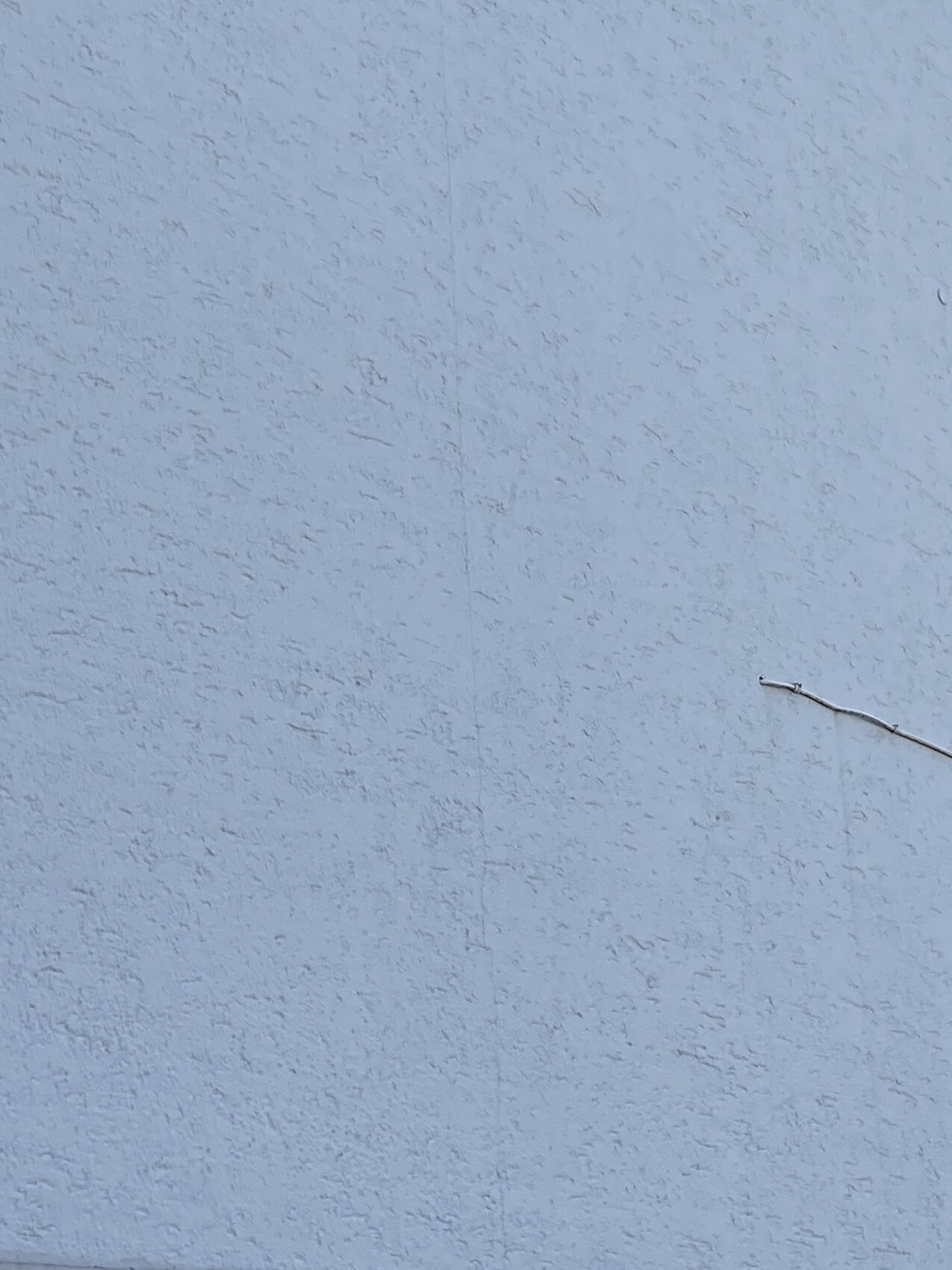 Hellblaue, grob strukturierte Außenwand; rechts eine dünne Leitung.