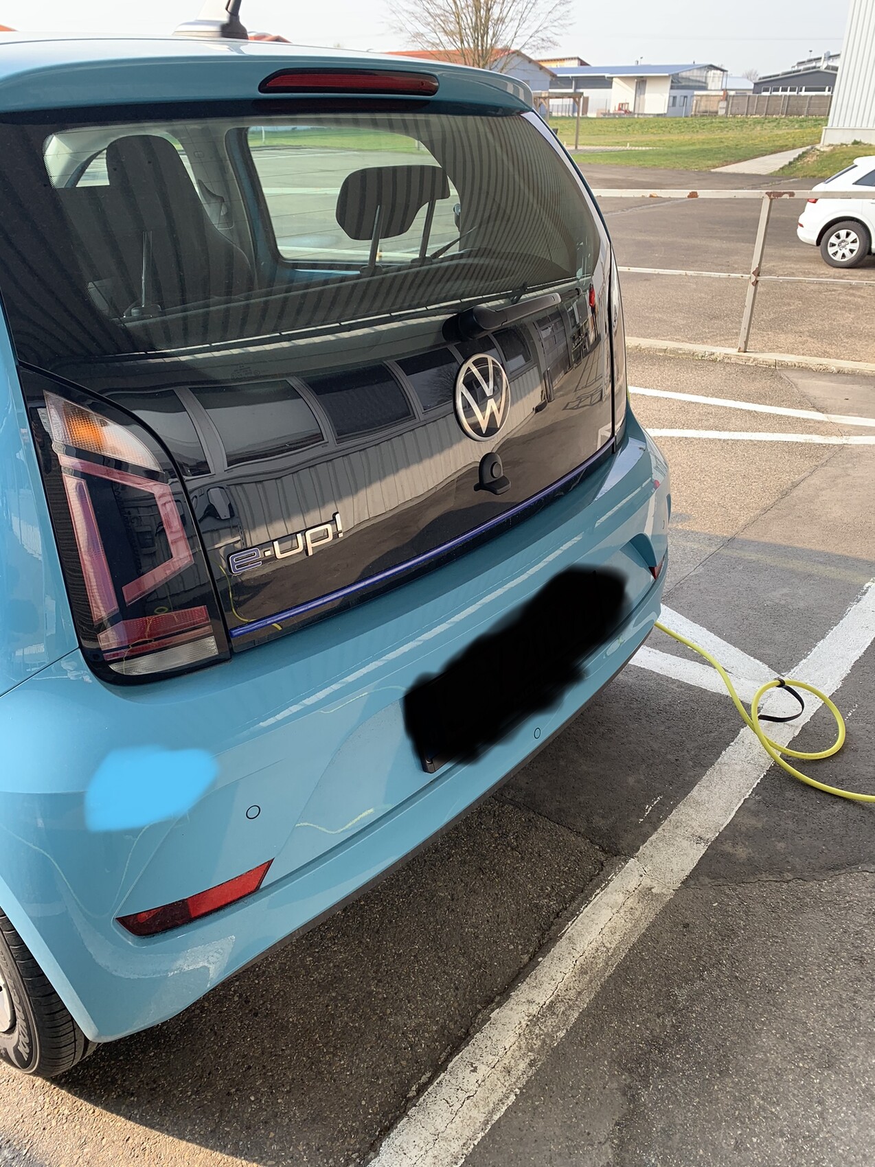 Rückansicht eines blauen VW e-Up! in einer Parklücke, Ladekabel angeschlossen.