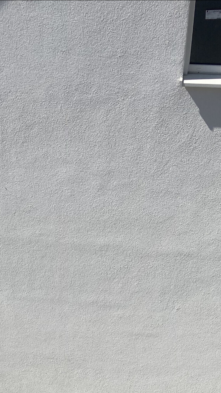 Grau texturierte Außenwand mit kleinem dunklem Fenster oben rechts.