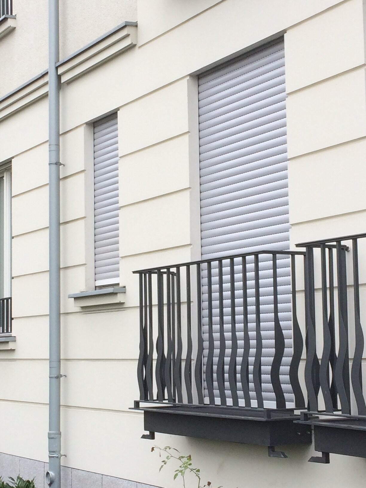 Außenansicht einer hellen Fassadenfront mit geschlossenen Rolläden und Balkon.