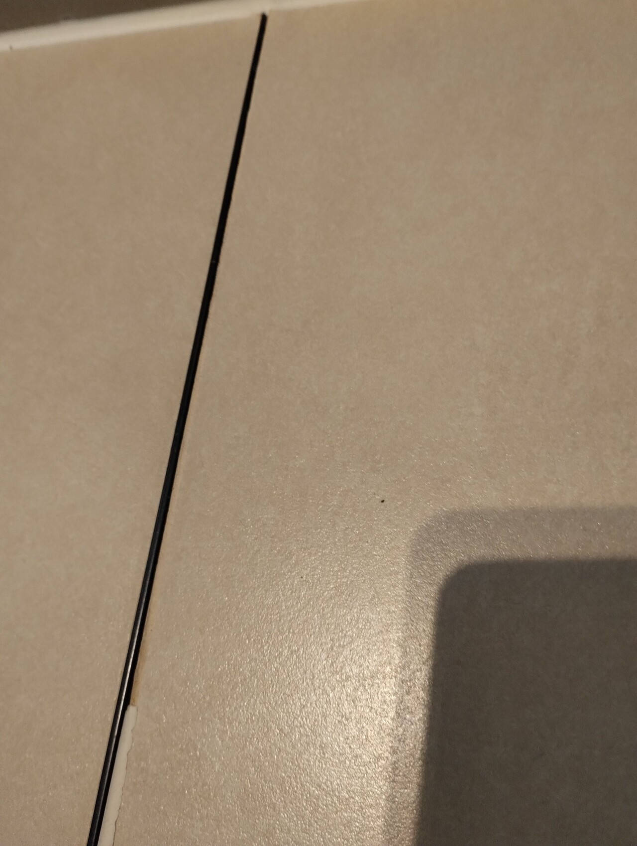 Nahaufnahme heller Bodenfliesen mit dunkler Fugenlinie und Schatten eines Geräts