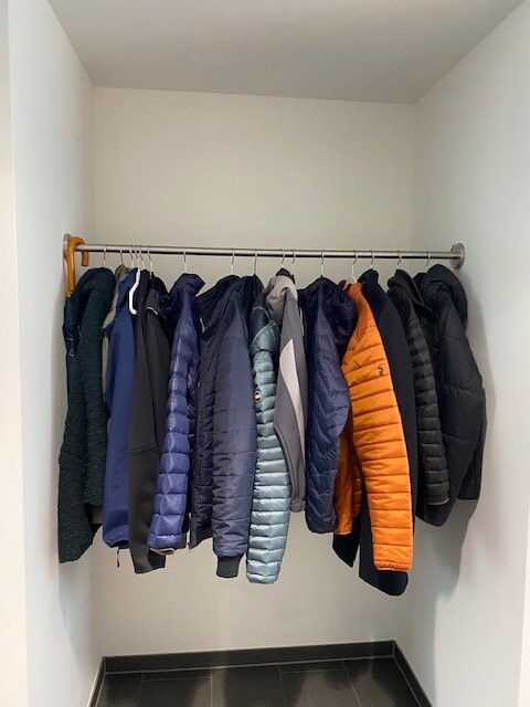Kleiderschrank mit Hängestange und bunten Winterjacken an Kleiderbügeln aufgehängt