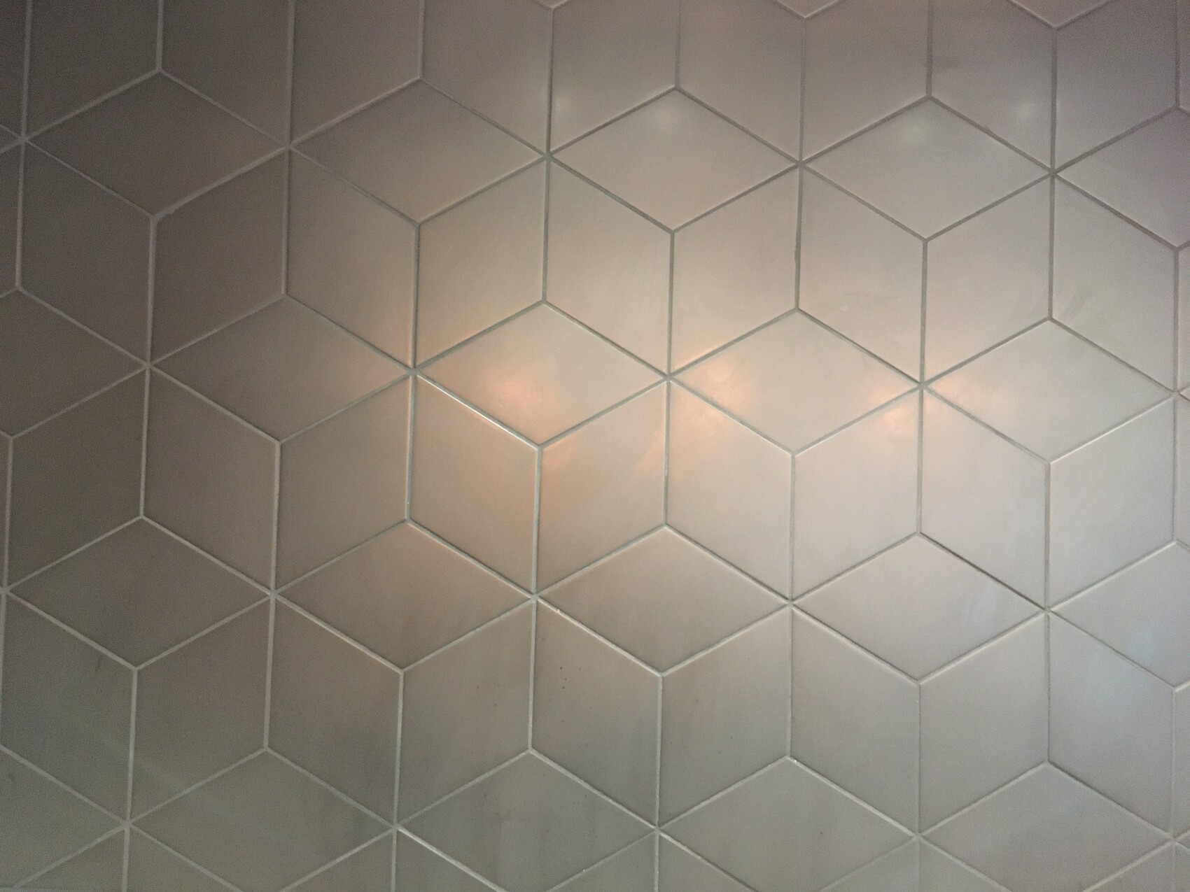 Hellgraue Wandfliesen mit hexagonalem Muster und hellen Fugenlinien.