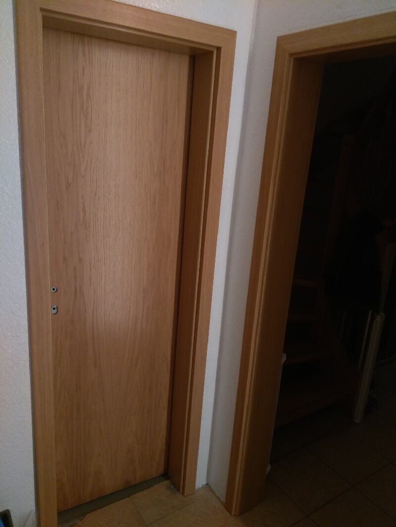 Zwei helle Holztüren im Flur; linke Tür geschlossen, rechte offen mit dunklem Raum dahinter.