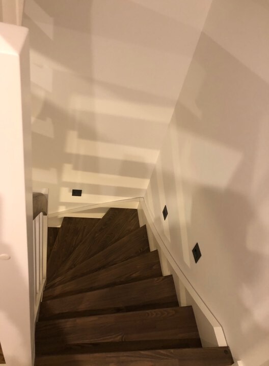 Dunkle Holztreppen führen nach unten; weiße Wände, Blick von oben auf die enge Treppe.