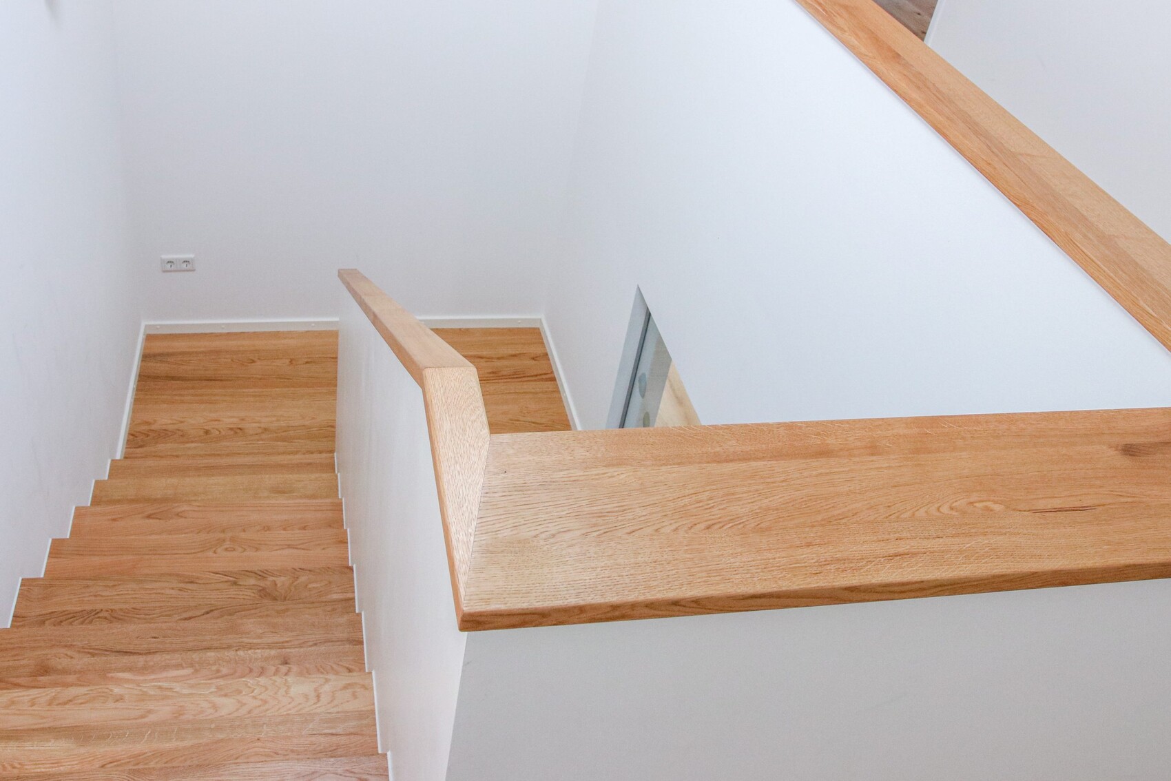 Innenraumtreppe aus Holz: von oben sichtbare Stufen, Geländer und weiße Wände.