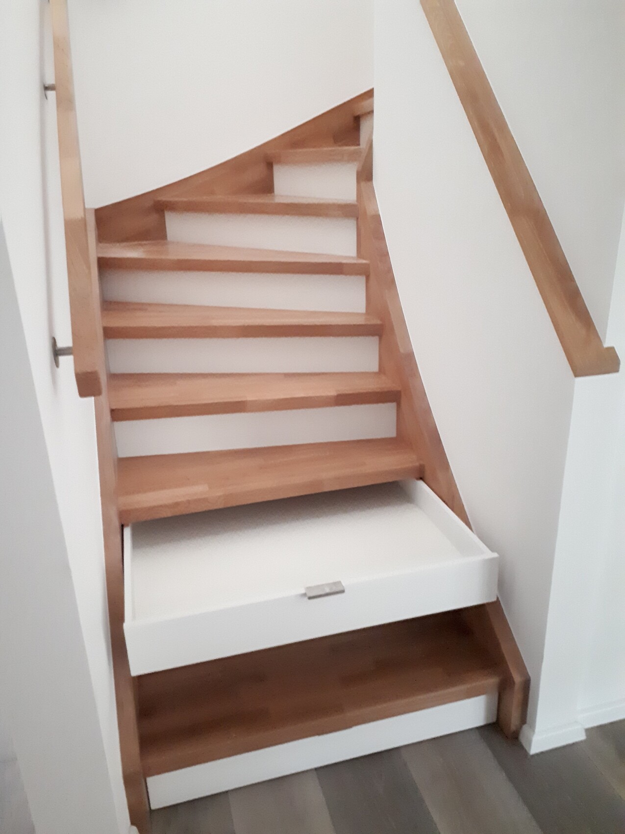 Moderne Holztreppe mit offenen Stufen; unten eine weiße Schublade ist herausgezogen.