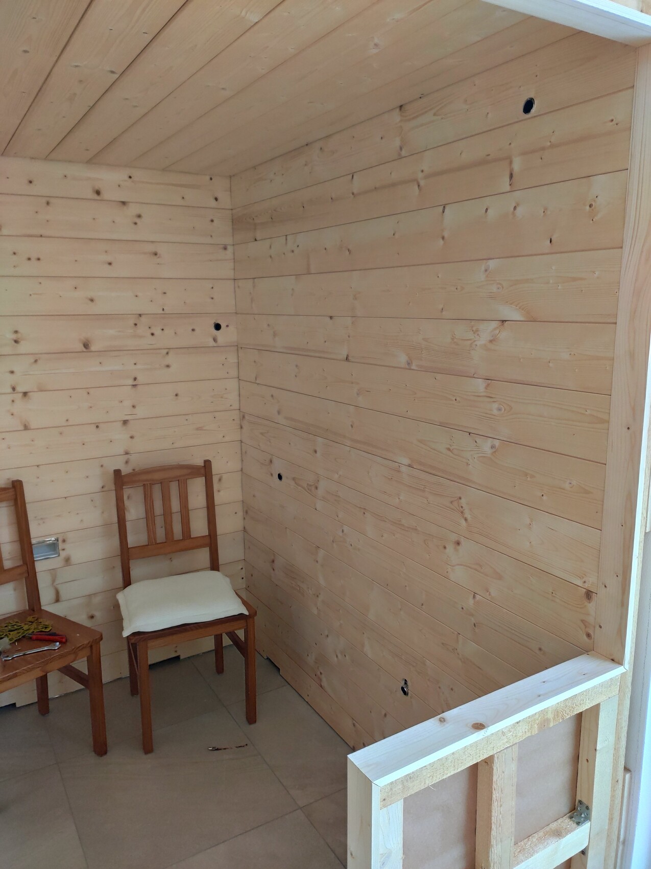 Holzverkleideter Innenraum mit zwei Holzhockern, weißem Kissen und Werkzeugen auf dem Tisch.