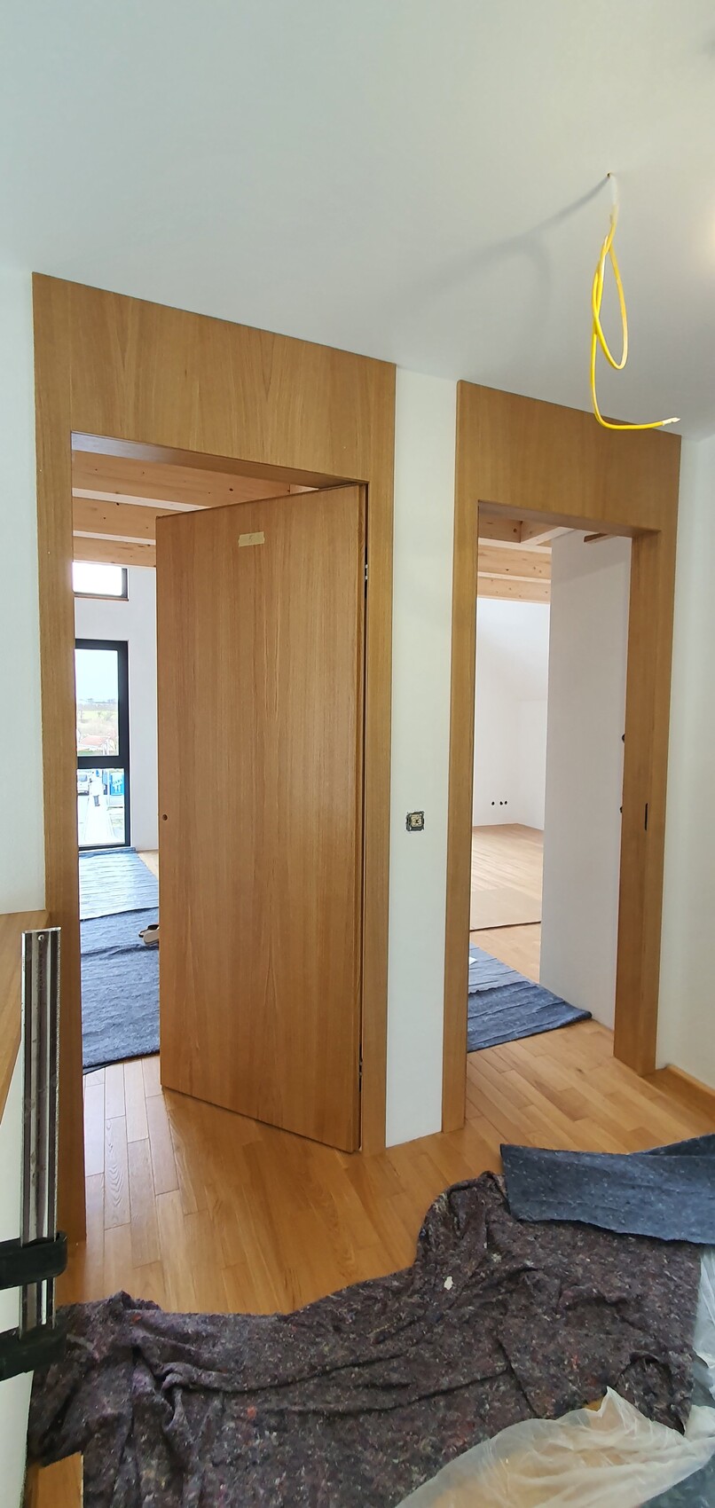 Flur mit zwei offenen Holztüren, Holzfußboden und gelben Kabeln von der Decke während der Renovierung.
