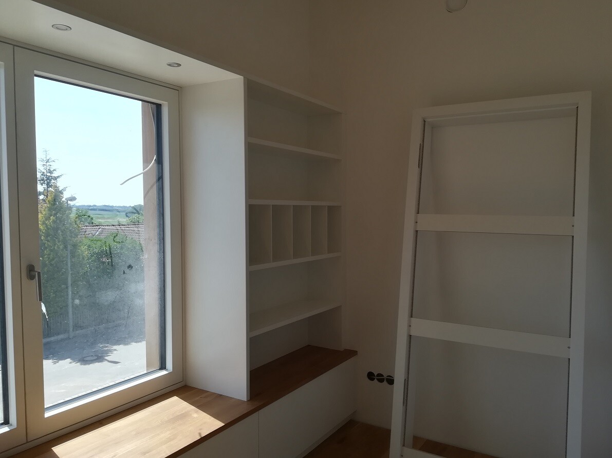 Heller Innenraum mit großem Fenster, weißem Regalsystem mit Fächern und Tür, die an der Wand lehnt