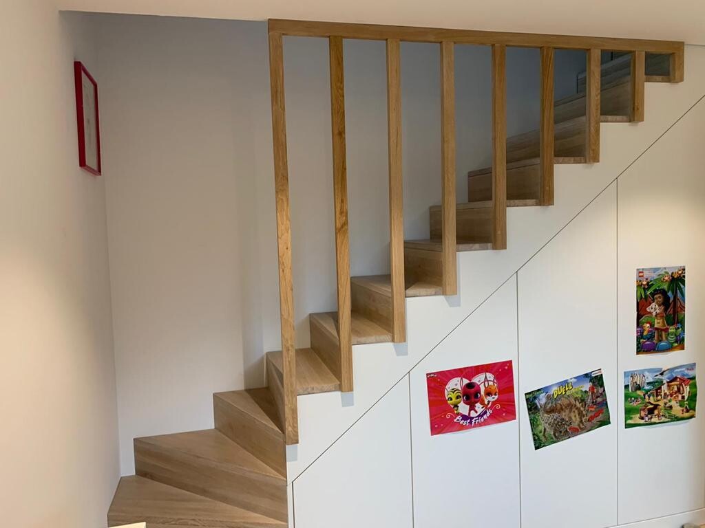 Offene Holztreppe mit Geländer neben weißen Schränken, bunten Postern; roter Bilderrahmen an der Wand