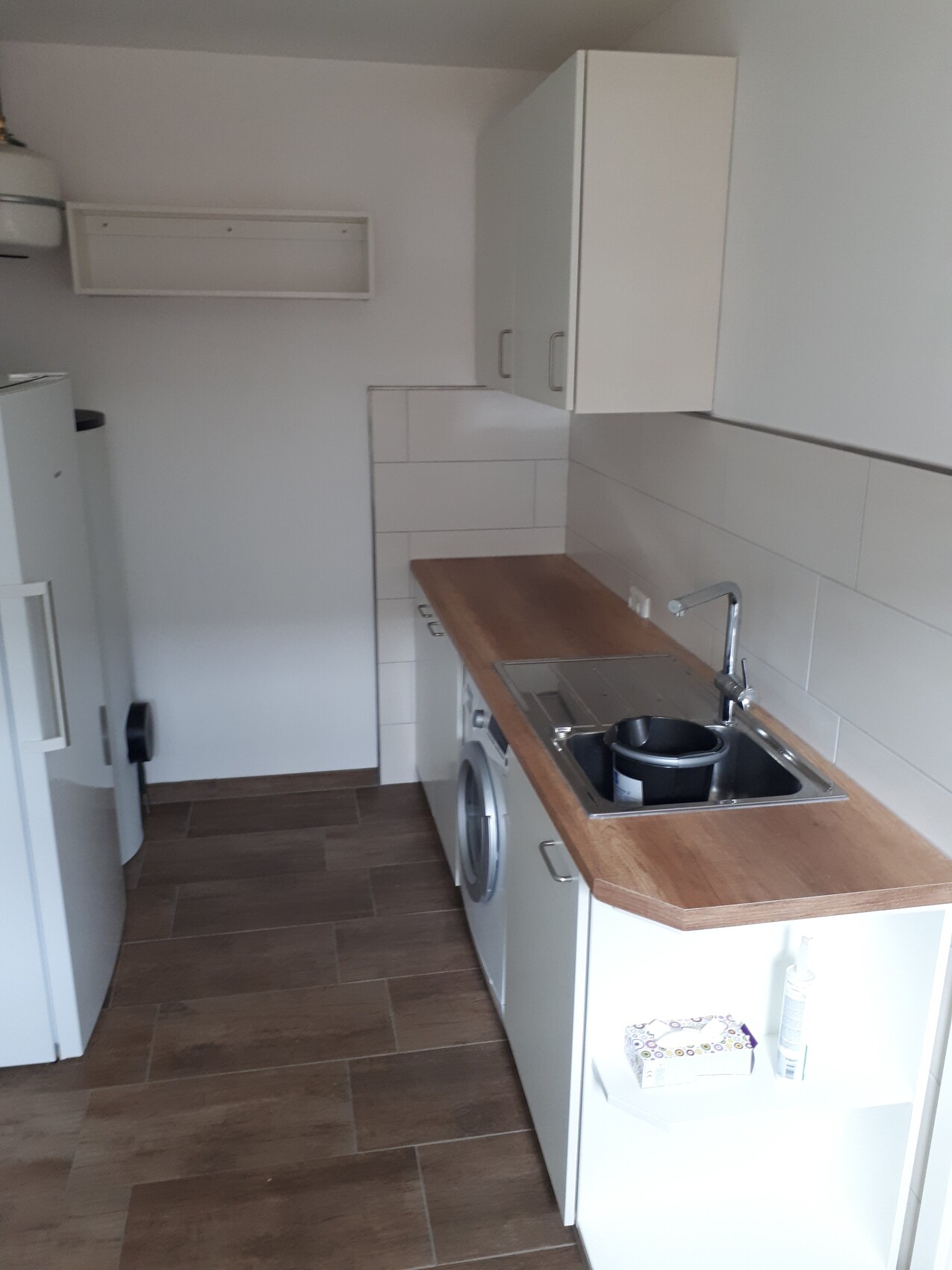 Kleine Küche mit Holz-Arbeitsplatte, Spüle, Waschmaschine, weißen Hängeschränken und Kühlschrank.
