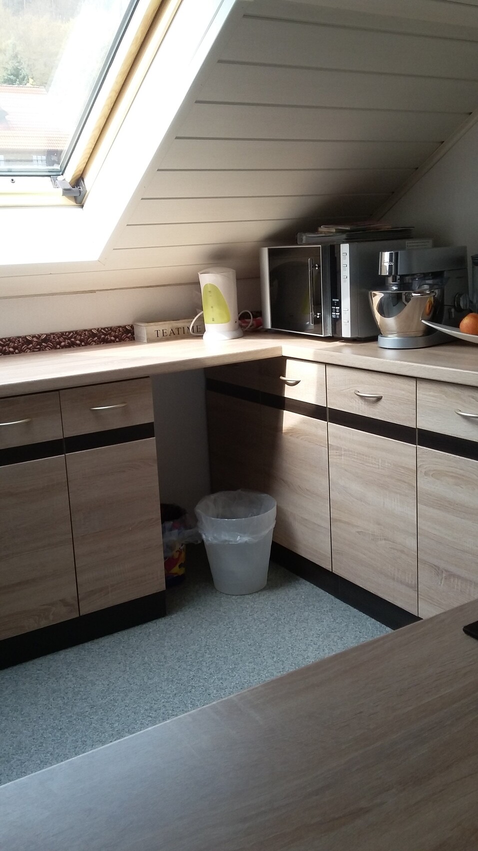 Küche mit schrägem Dachfenster, Mikrowelle, Mixer, Wasserkocher und Obst auf der Arbeitsfläche.