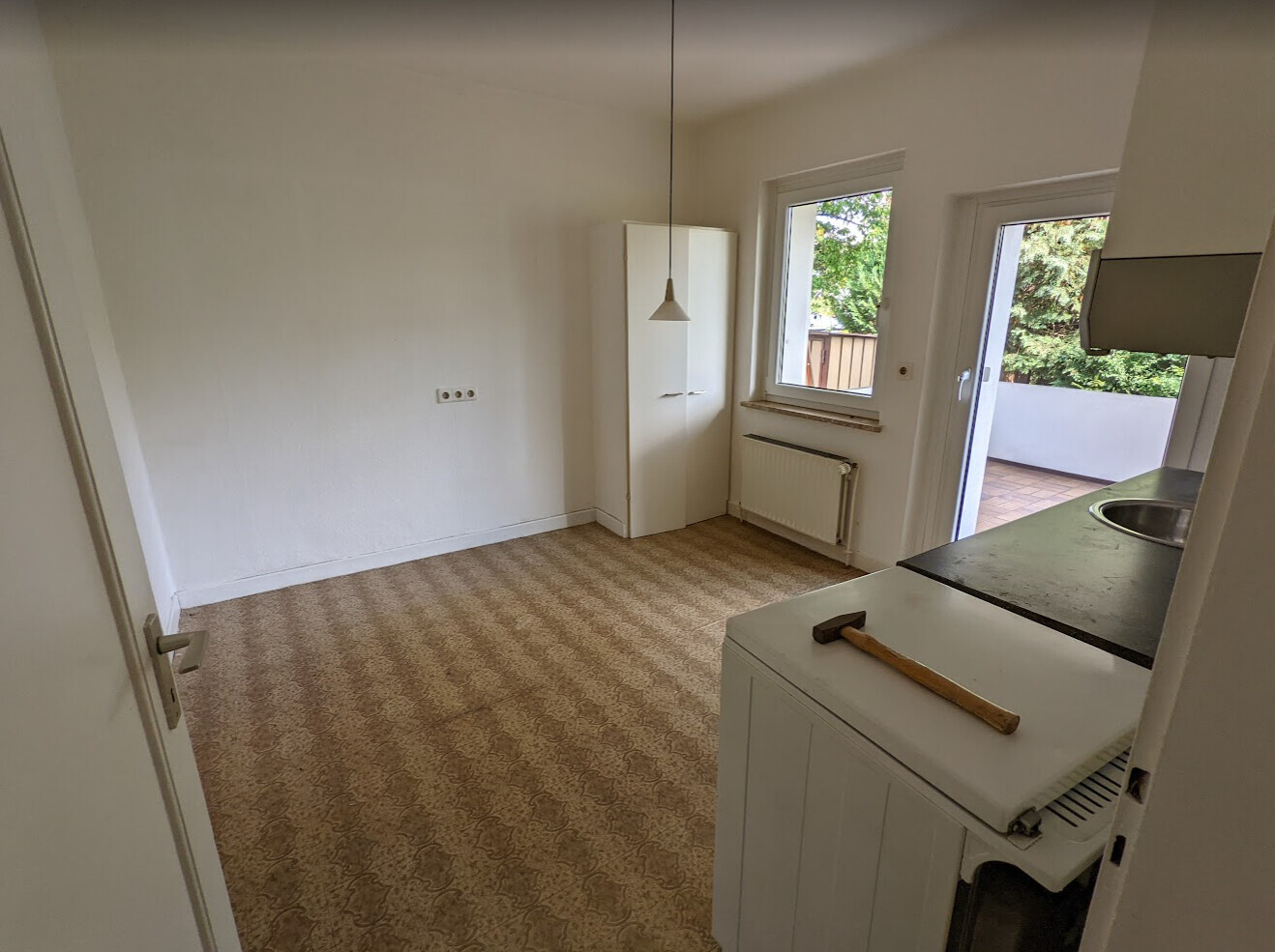 Leerer Raum mit beigem Teppich, weißem Schrank, Fenster und Tür zum Balkon, Axt auf Küchenschrank