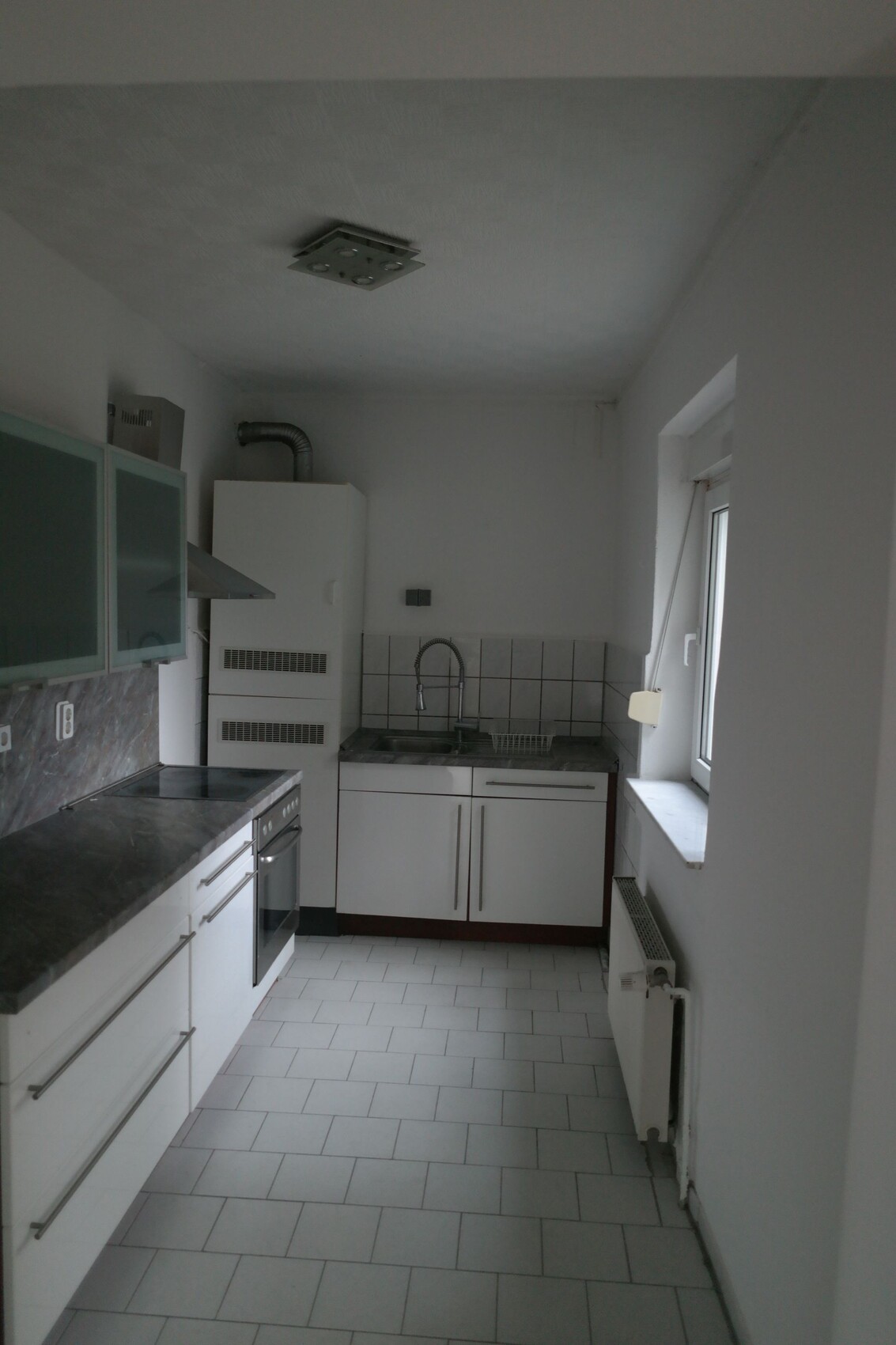Kleine moderne Küche mit Spüle, Herd, Dunstabzug, weißen Schränken und Fenster.