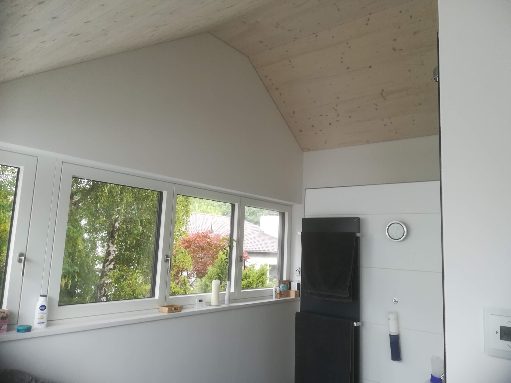 Helle Küche mit großen Fenstern, Holzdecke, schwarzer Ofen mit Handtuch, Uhr an der Wand.