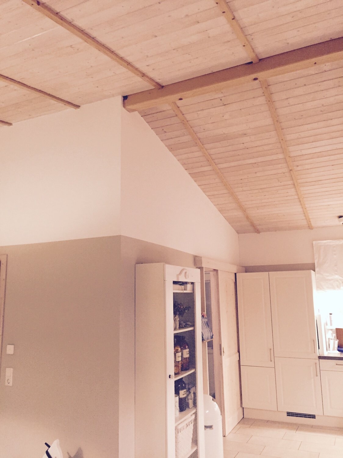 Küche mit weißen Schränken, Glastür-Schrank und sichtbarer Holzbalkendecke.