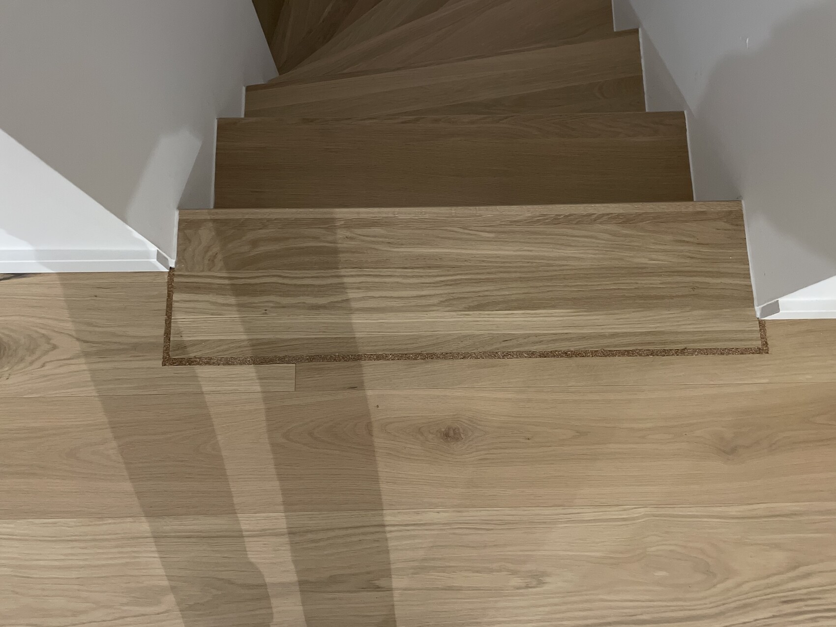 Holztreppe mit hellen Eichenstufen in Innenraum, weiße Wände, Blick von oben.