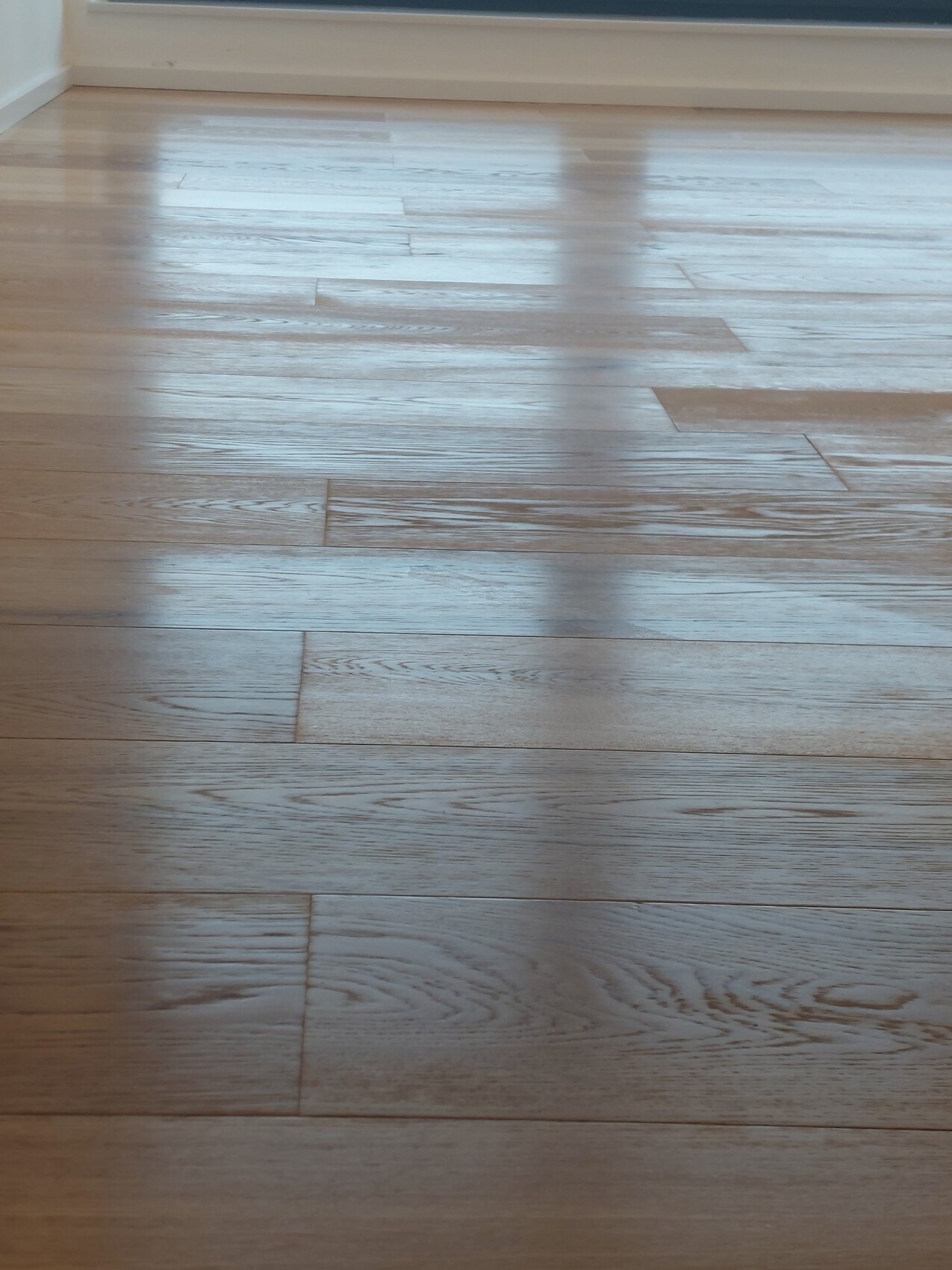 Heller Holzdielenboden mit sichtbarer Maserung und Lichtreflexen durch Fensterlicht.