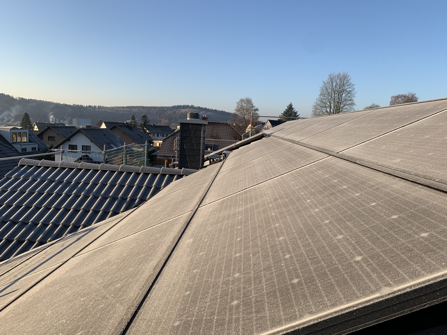 Dach mit Solarpanelen, Vorstadtblick auf Häuser, Bäume und blauen Himmel.