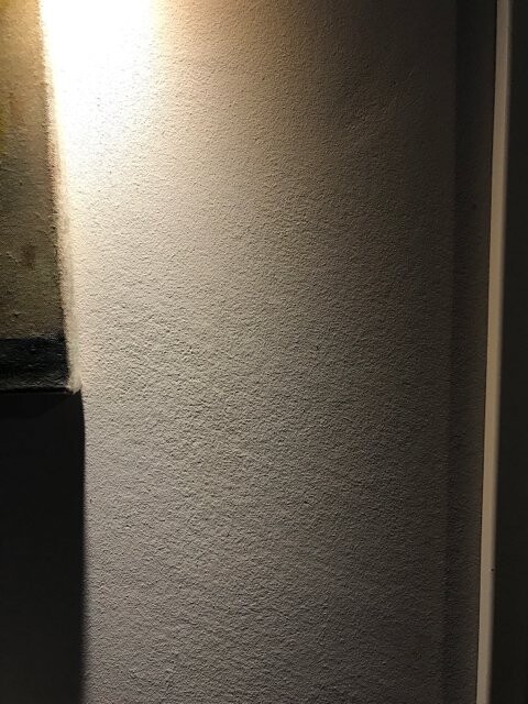 Nahaufnahme einer hellgrauen, rauen Putzoberfläche einer Säule, seitlich beleuchtet.
