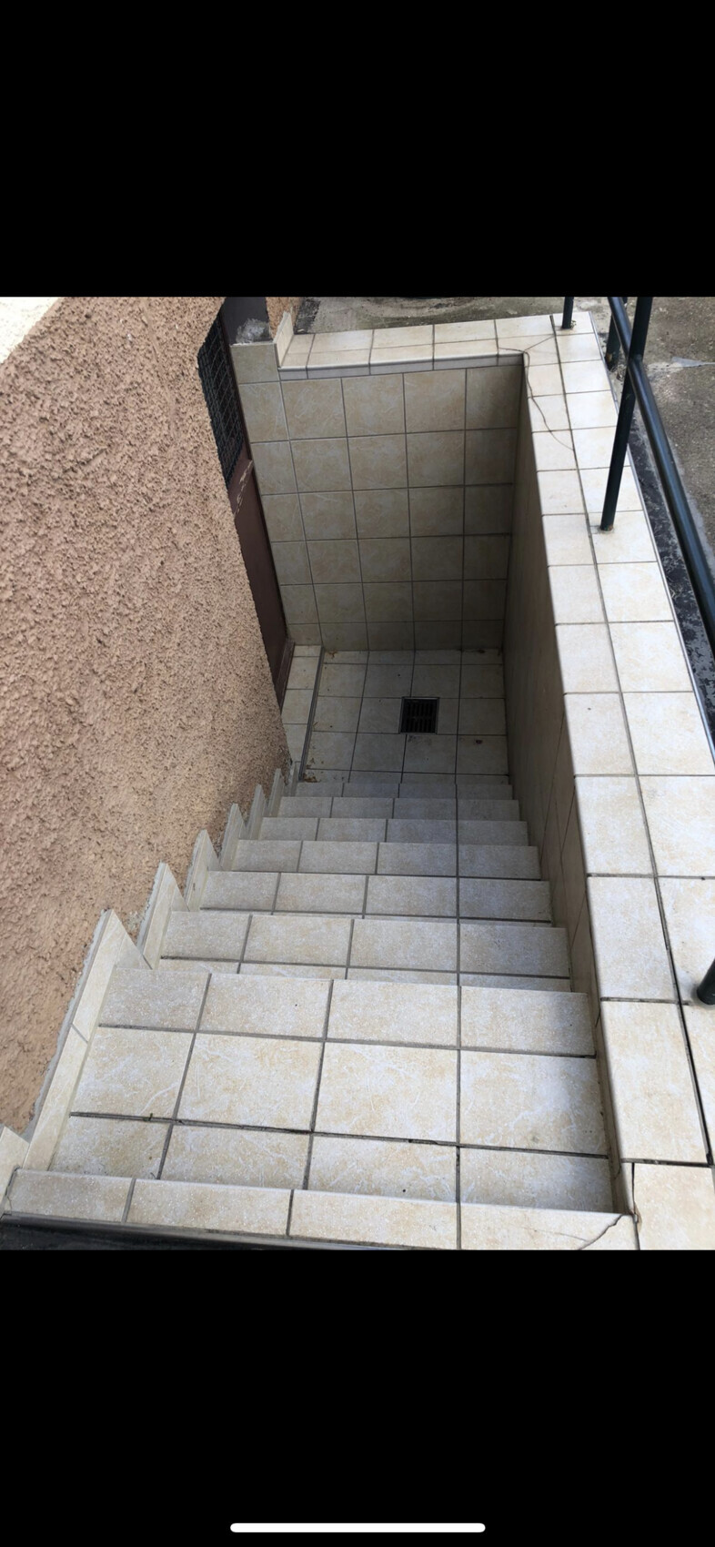 Stufen einer Außentreppe mit hellen Fliesen, rechts Geländer, unten Abfluss im Boden.