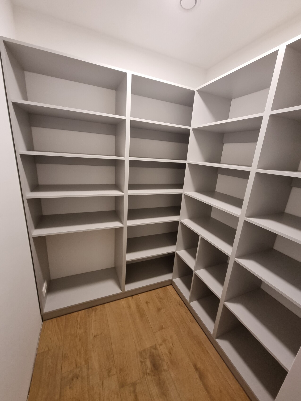 Begehbarer Kleiderschrank mit vielen leeren weißen Regalen an drei Wänden, Holzfußboden.