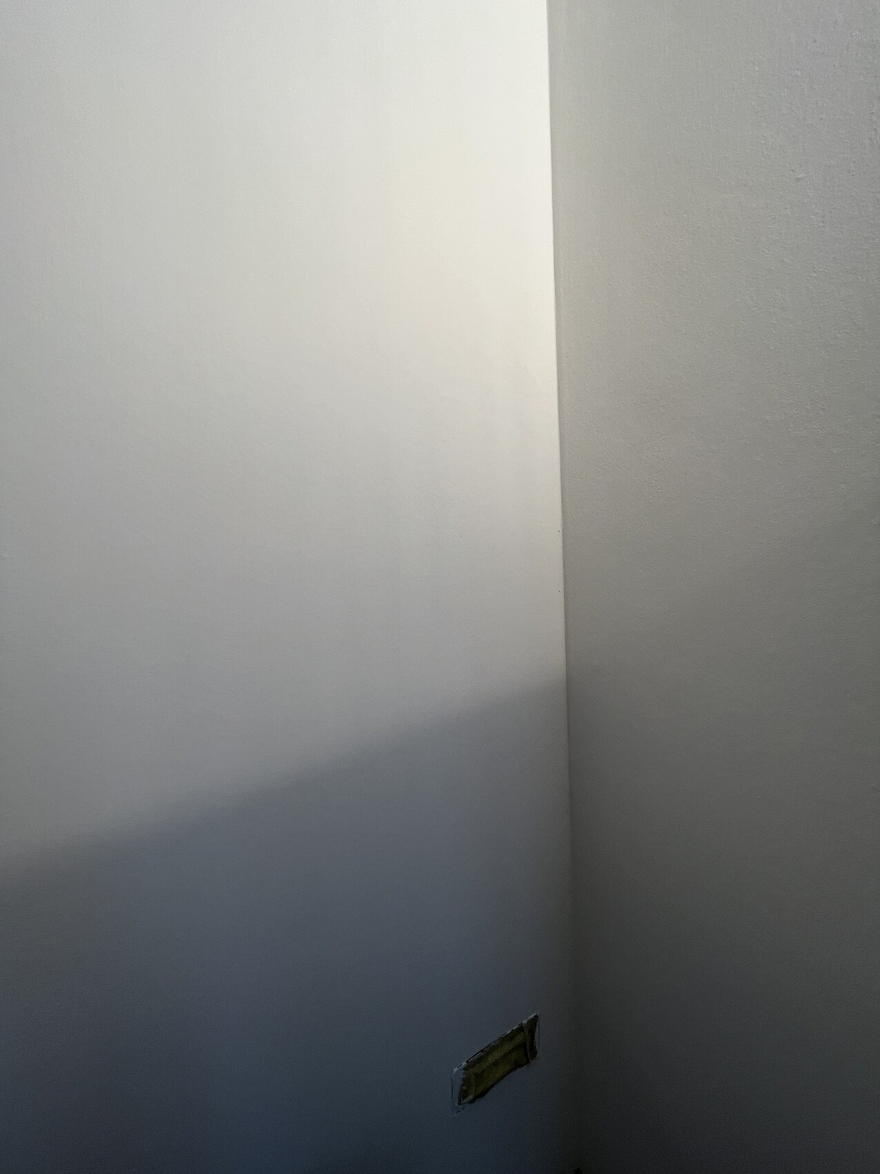 Zwei weiße Wände treffen sich in einer Innenraum-Ecke; unten rechts offene Steckdosenöffnung