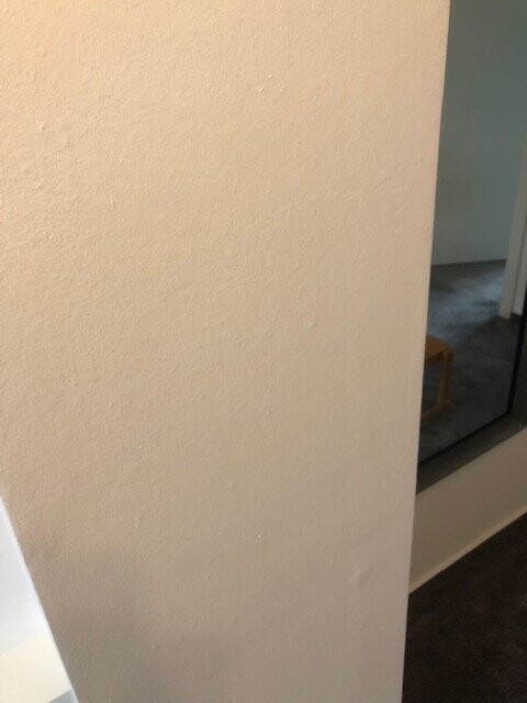 Beige Innenwand im Vordergrund; rechts Spiegel, dunkler Boden, hintere Ecke sichtbar.