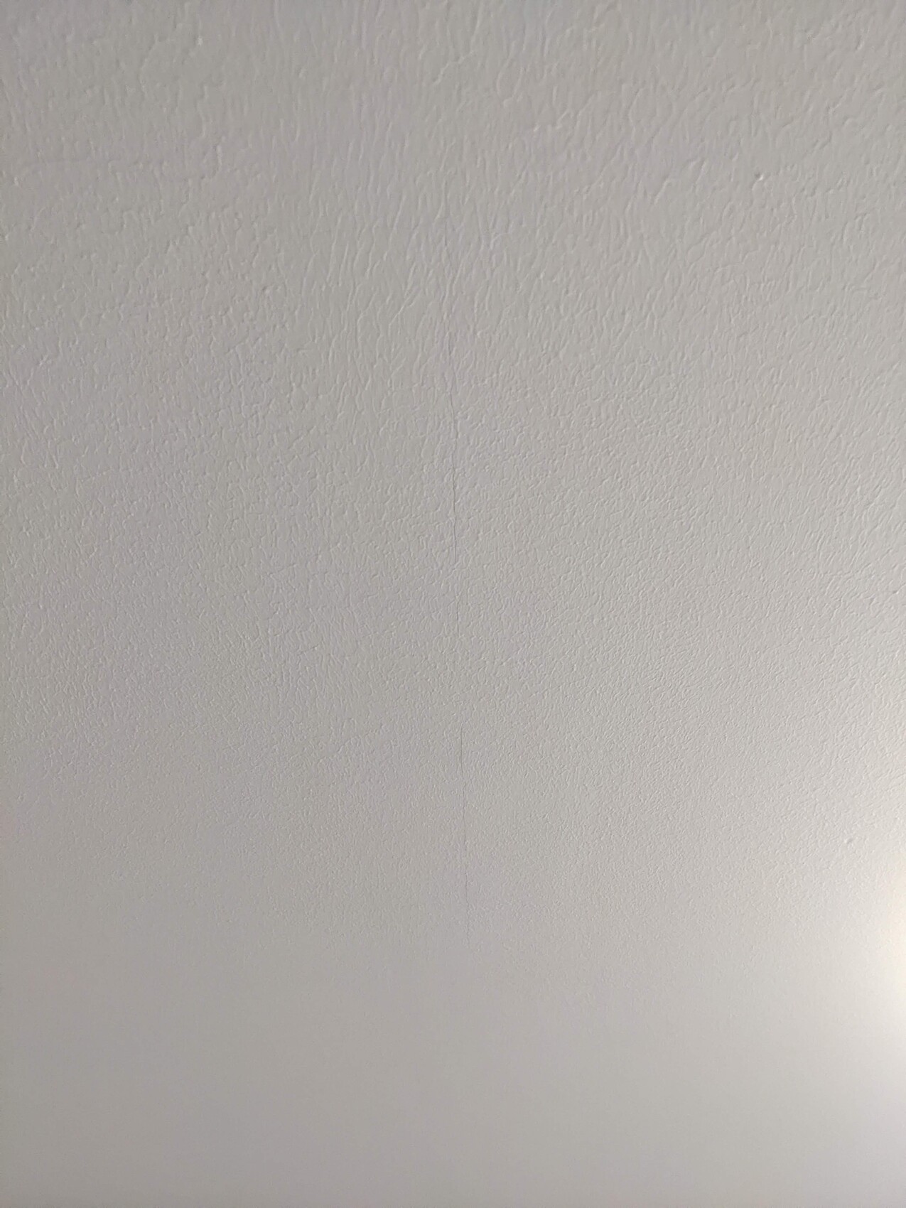 Weiße, texturierte Wand/Decke mit feiner Putzstruktur und leichter Lichtkante unten rechts.