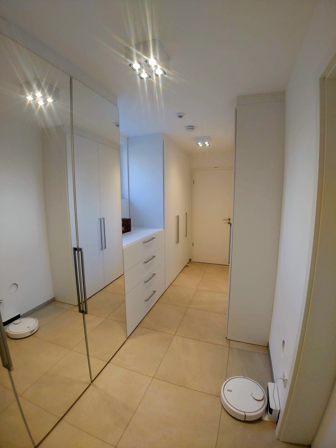 Heller begehbarer, weißer Kleiderschrank mit Spiegelfronten und zwei Saugrobotern.