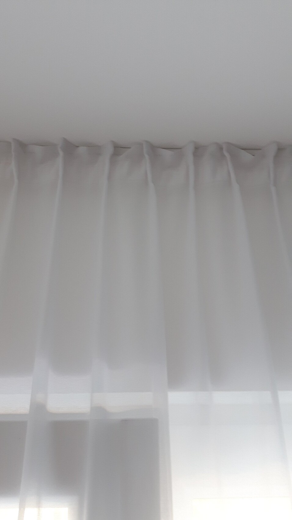 Transparente weiße Vorhänge hängen vor Fenstern; sanftes Licht filtert ins Zimmer.
