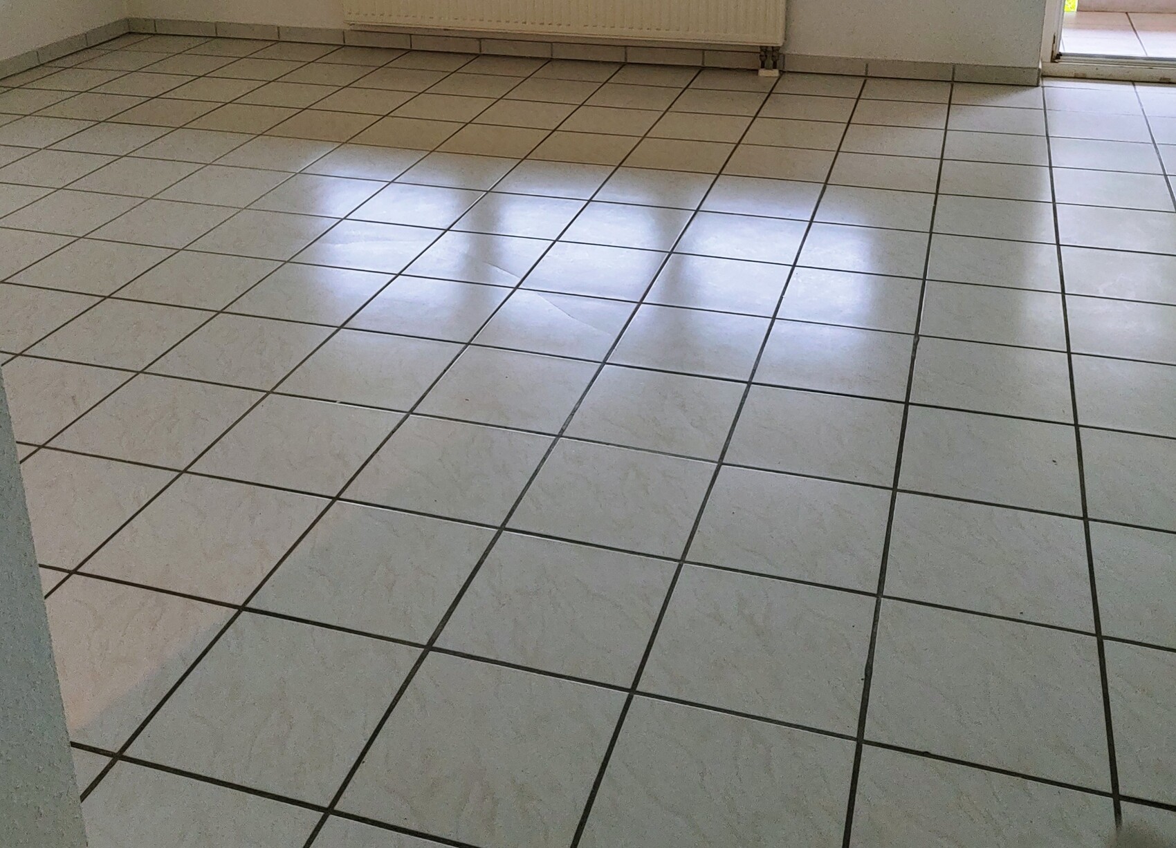 Weiße quadratische Bodenfliesen in Innenraum; Lichtreflexe auf dem Boden.