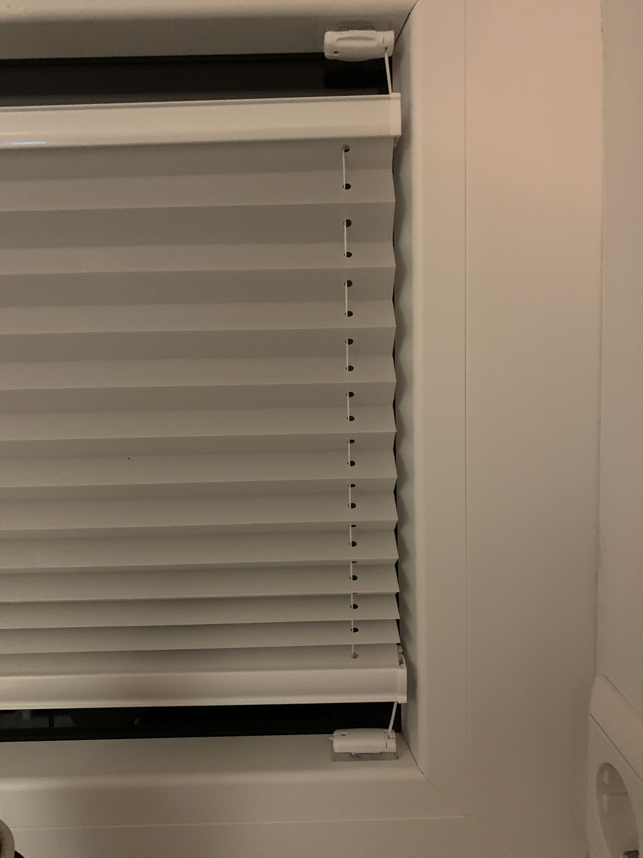 Weiße Fensterjalousie mit horizontalen Lamellen im Rahmen; seitliche Zugkordel sichtbar.