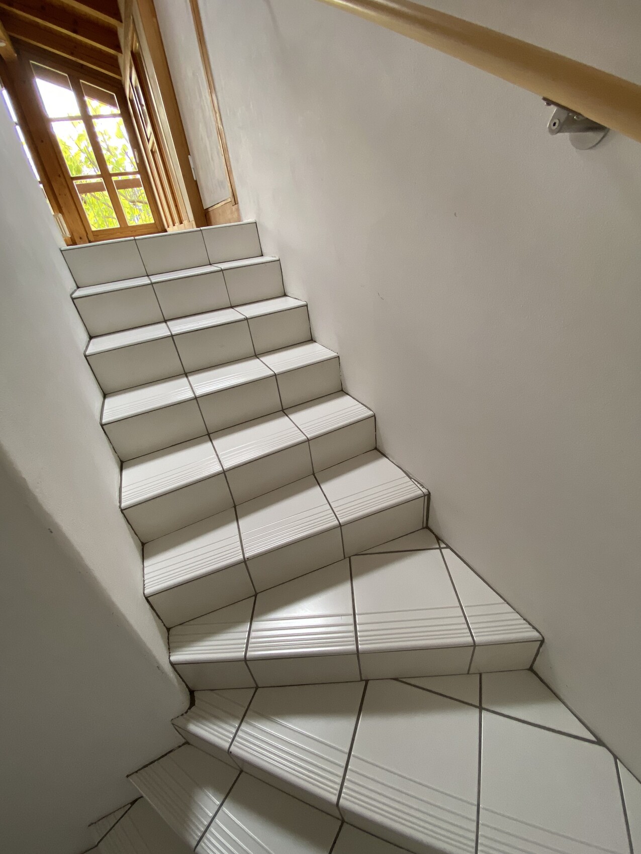 Helle Innen-Treppe mit weißen, geriffelten Fliesenstufen; Fenster oben lässt Licht herein.