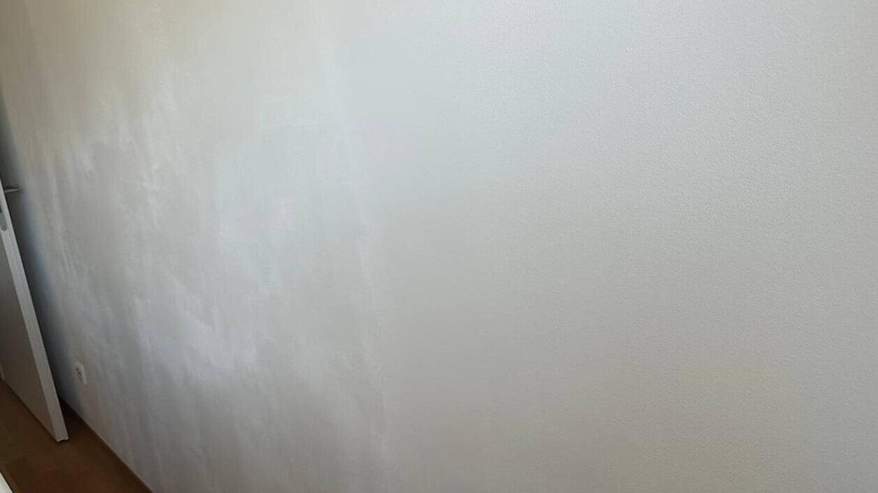 Weiße Innenwand mit unregelmäßigen Verfärbungen und Flecken; Holzboden unten.