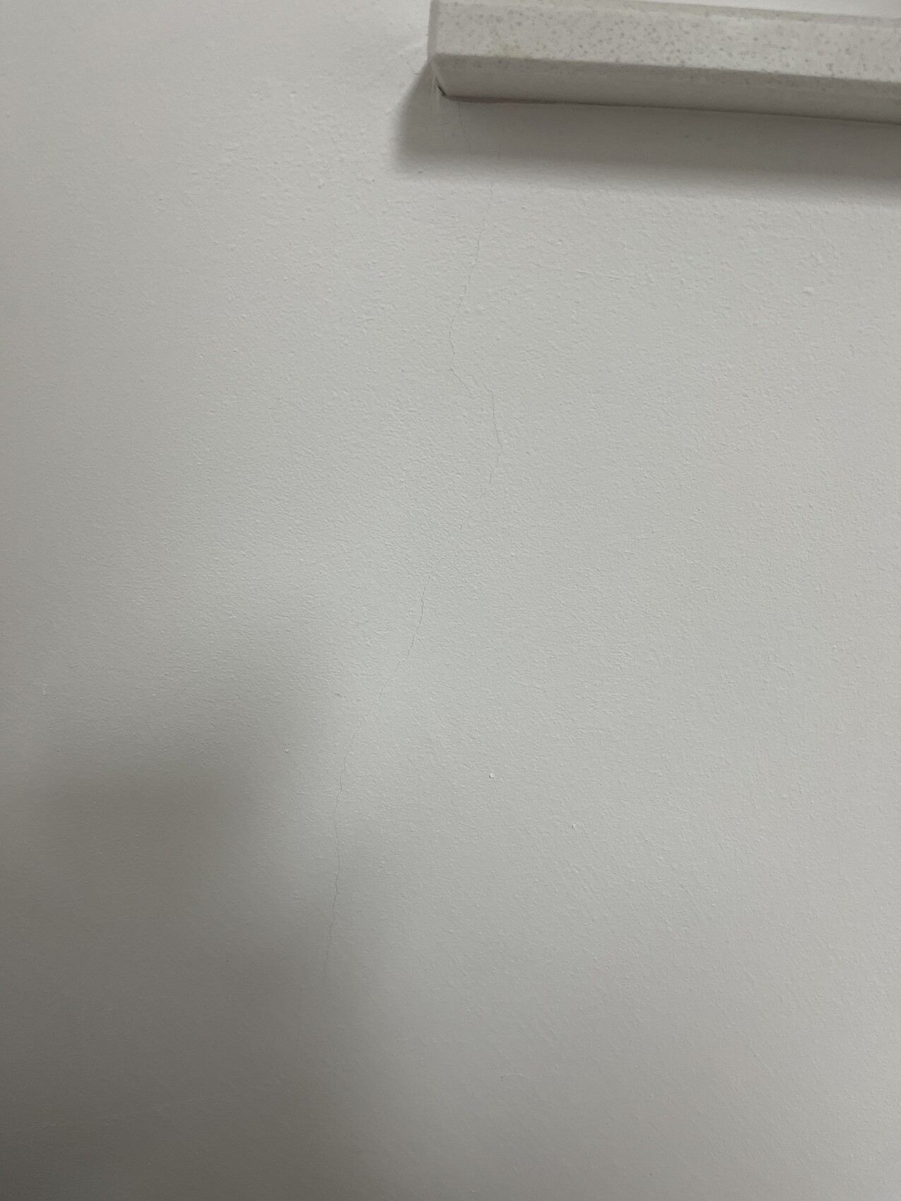 Weiße Wand mit feiner Risslinie; oben eine kleine horizontale Leiste sichtbar.