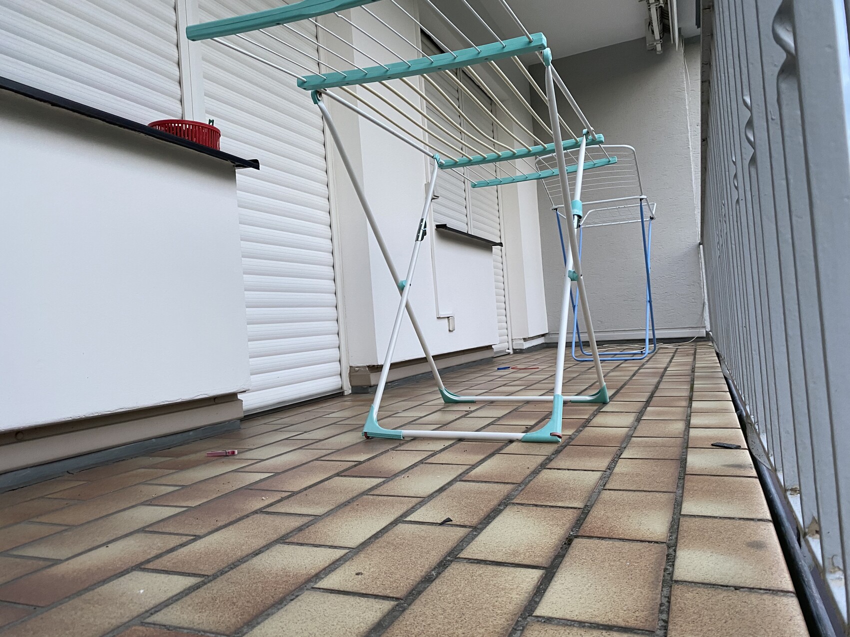 Zwei Metall-Wäscheständer auf Balkon mit Fliesenboden, türkis-weiß; roter Korb auf Ablage.