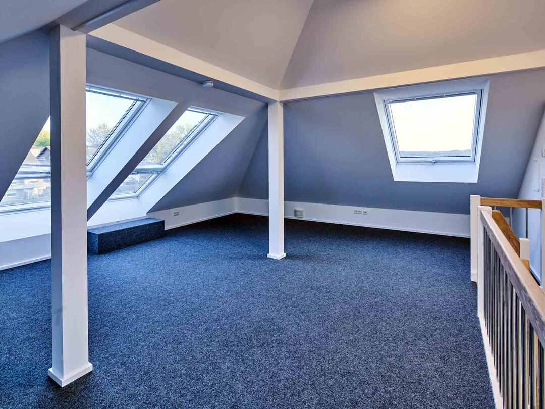 Heller Dachbodenraum mit blauen Wänden, Dachfenstern, Treppengeländer und Teppich.