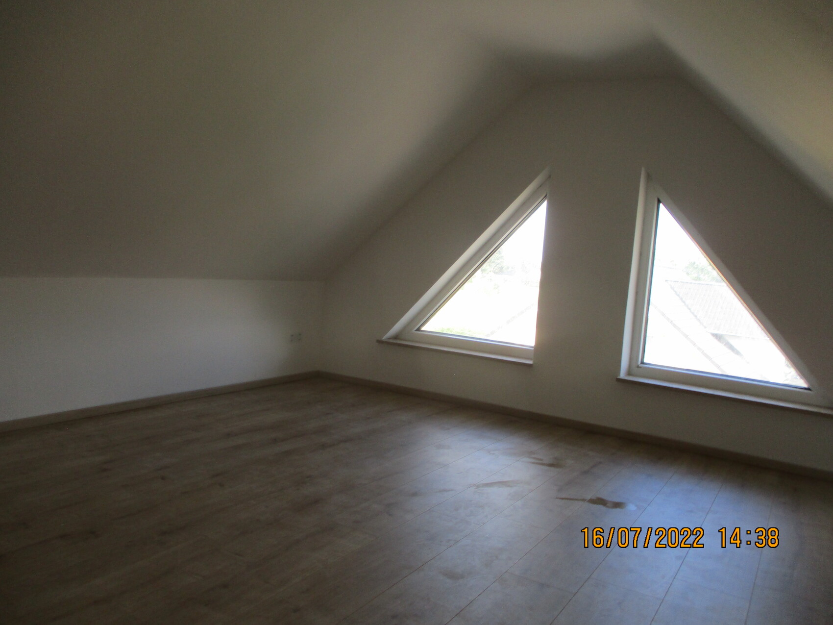 Leeres Dachgeschosszimmer mit zwei dreieckigen Dachfenstern, Holzfußboden, helle Wände.