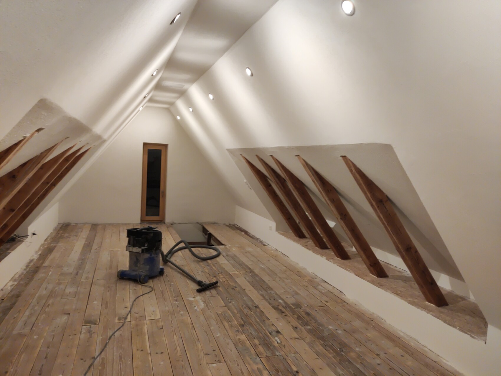 Dachgeschoss im Ausbau mit schrägen Wänden, freiliegenden Balken und Staubsauger.