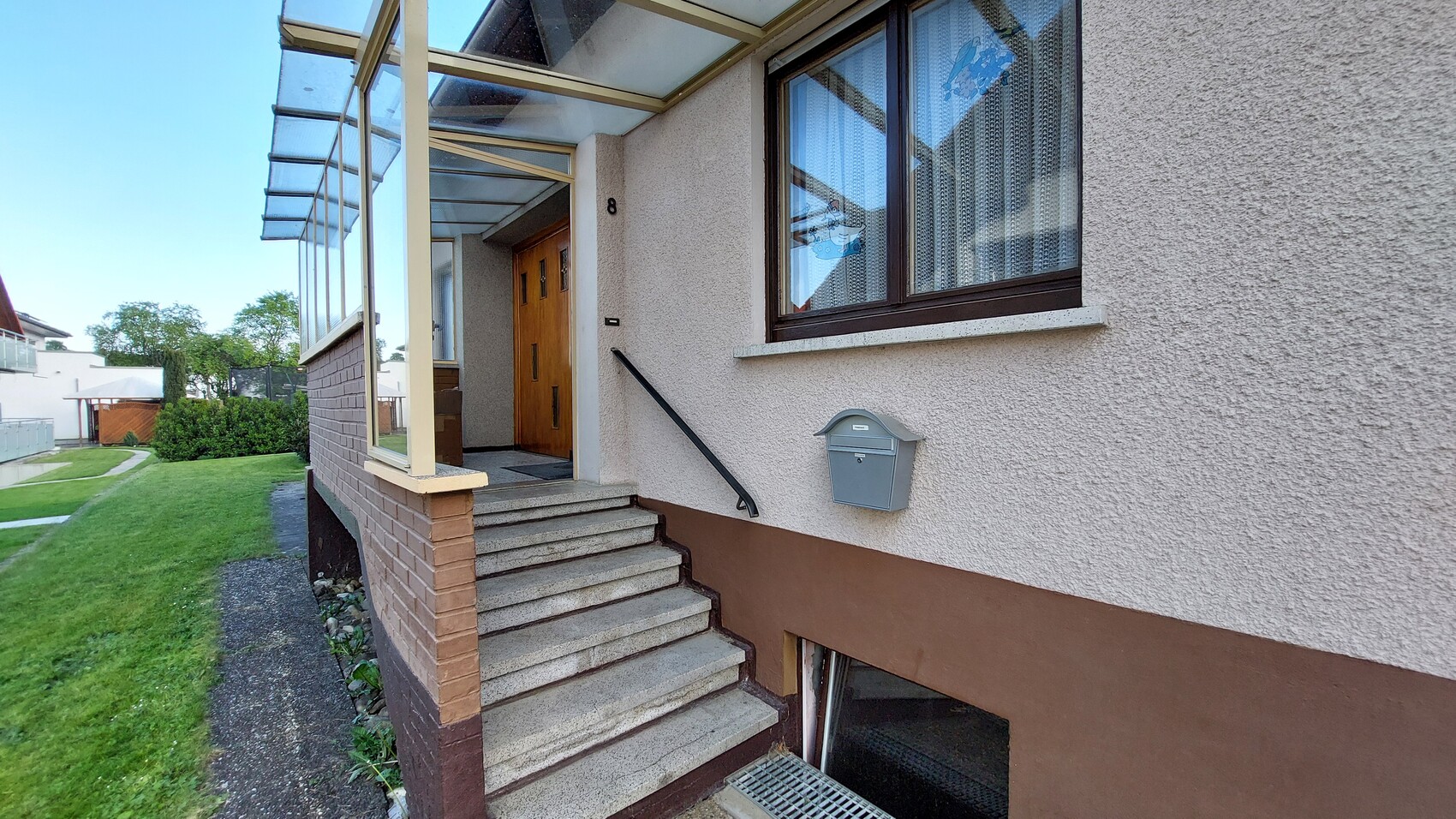 Außeneingang eines Wohnhauses: Treppe, Geländer, Tür Nr. 8, Briefkasten und Fenster mit Vorhängen.
