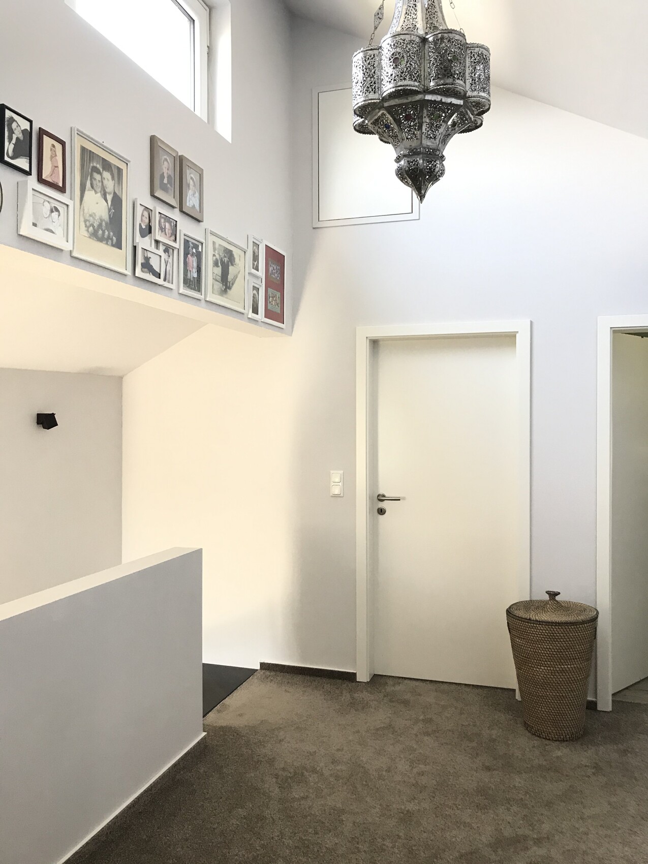 Heller Flur mit Bildergalerie an der Wand, großer metallischer Kronleuchter, Tür und Korb.