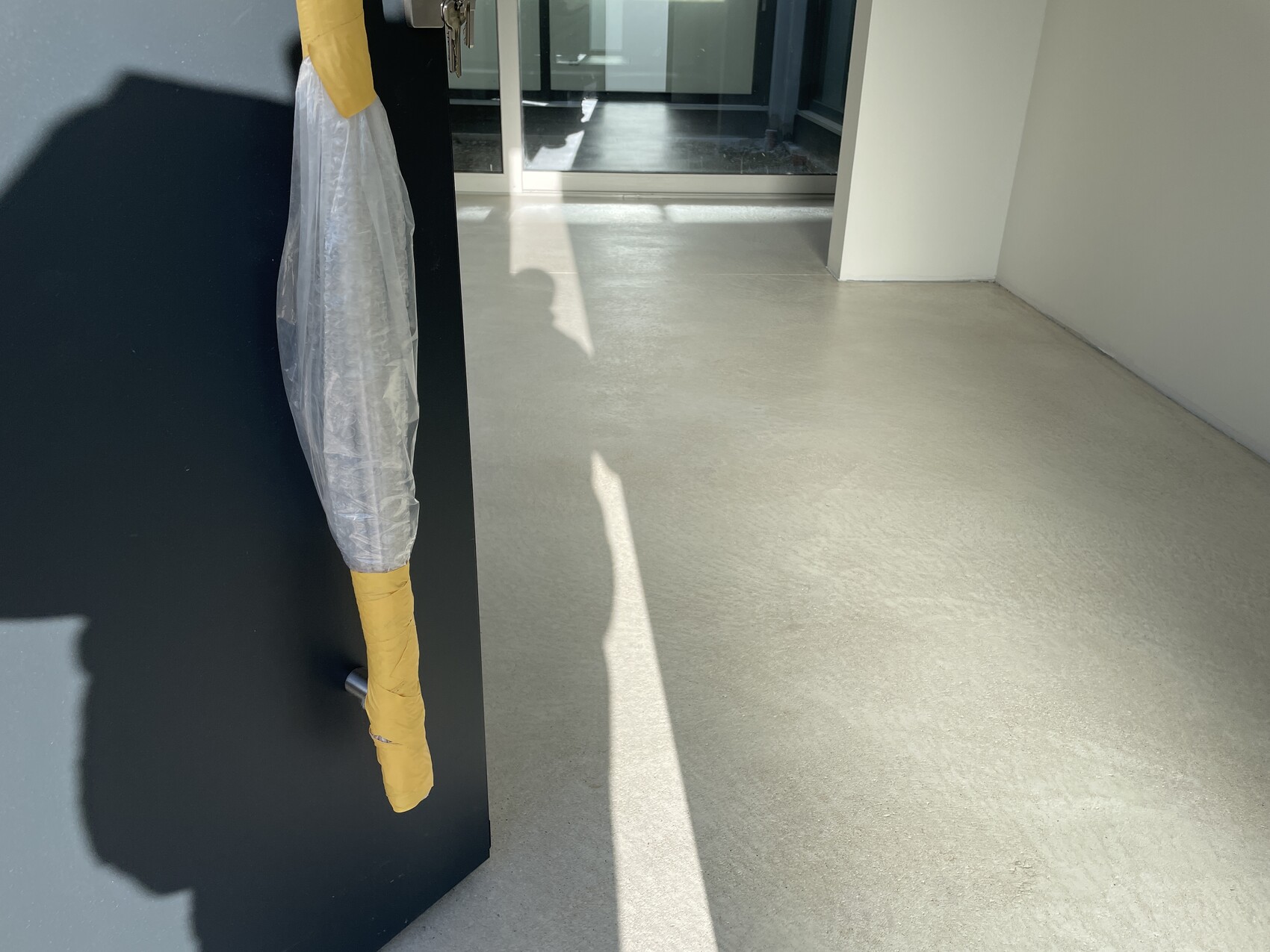 Schmaler Flur; dunkle Wand links, eingewickelter Gegenstand in Plastikfolie mit gelbem Klebeband.
