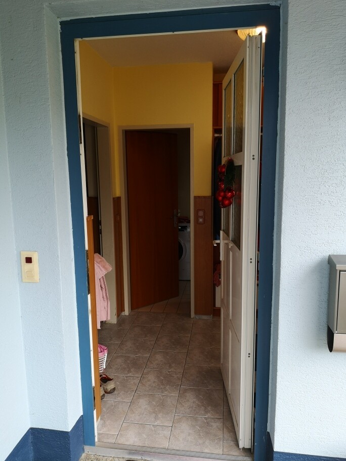 Offene Haustür führt in den Flur mit Fliesenboden gelbe Wände und Waschmaschine sichtbar.